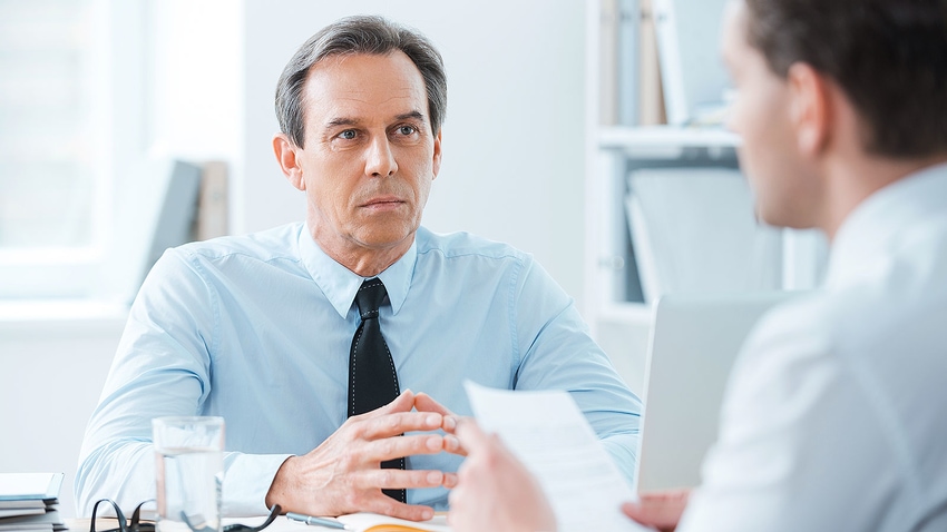 Frowning boss at desk looks skeptical during difficult discussion with employee about legal trouble